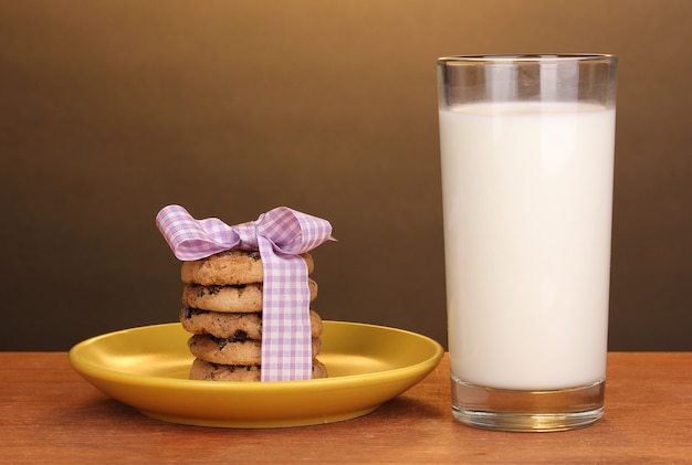 Glass of milk and cookies on wooden table on brown background