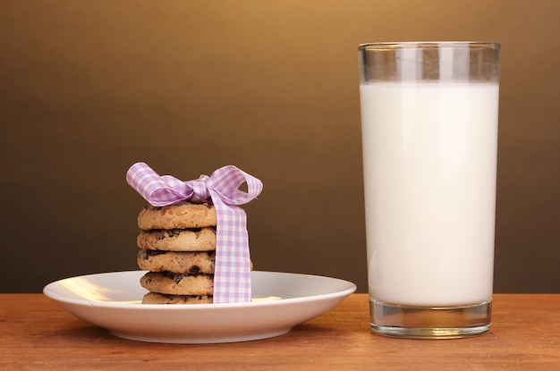 Glass of milk and cookies on wooden table on brown background