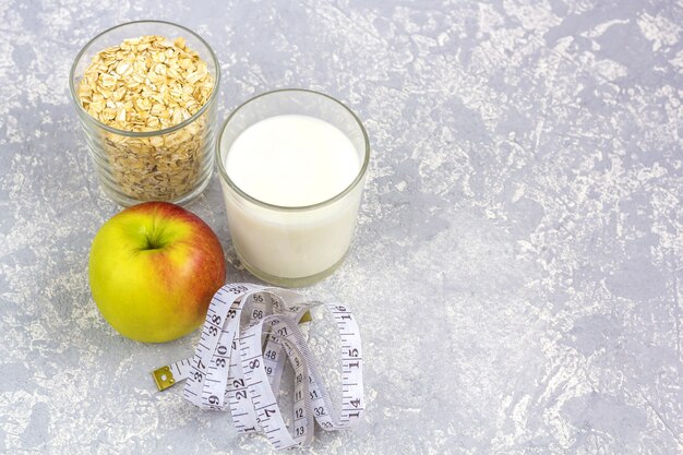 A glass of milk and a glass of oat flakes (rolled oats). Apple with measuring tape.