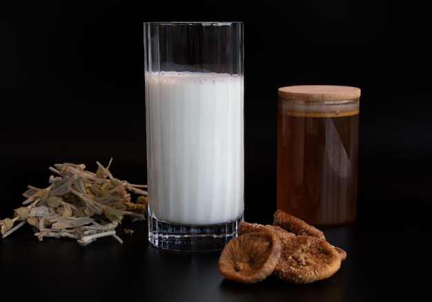 glass of milk honey medicinal herbal tea and dried fig on the black background