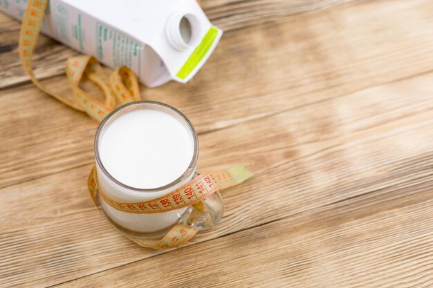 A glass of milk kefir and a measuring tape on a wooden background The concept of diet weight loss