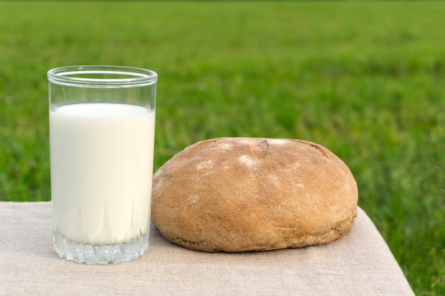 A glass of milk and a loaf of rustic bread against the background of a blurred meadow