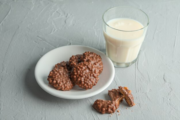 Glass of milk and plate with chocolate cookies on grey table,