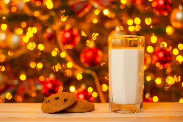 Glass of milk and some cookies on table on background of\
christmas lights milk and snack for santa concept