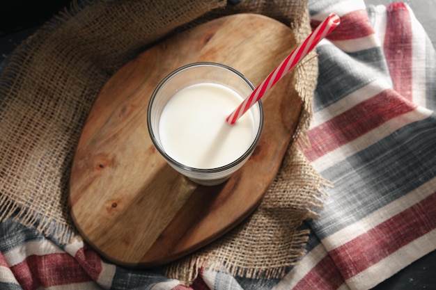 Glass of milk with straw on wooden board top view