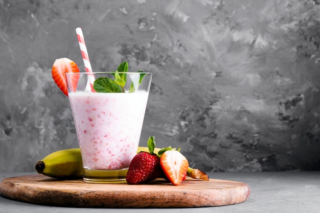 Glass of milkshake with strawberries and mint on a concrete surface