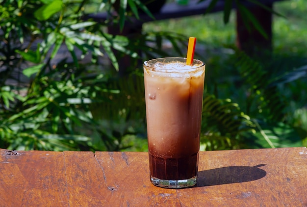 A glass of milkshake on a wooden table in the park.