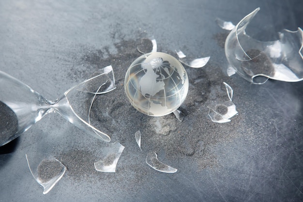 Glass model of the planet against the background of a broken hourglass The concept of stopping time for the life of the earth