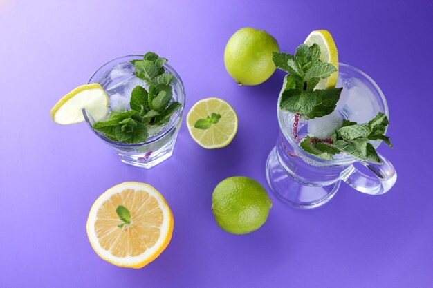 Glass of mojito with ice and mint Closeup of cocktails with different types of citrus fruits on a purple background