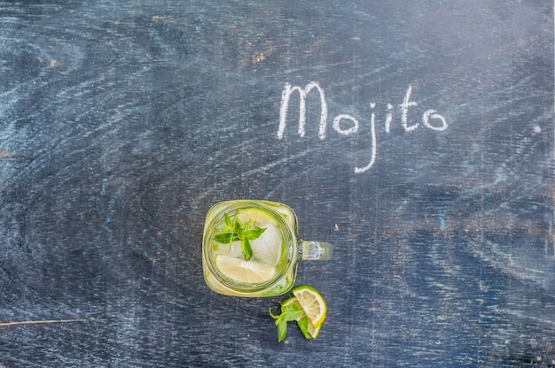 Glass of mojito with lime and mint ice cube close-up on dark wood surface