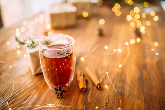 Photo glass mug of black tea with star anise on the wooden festive table with garland lights