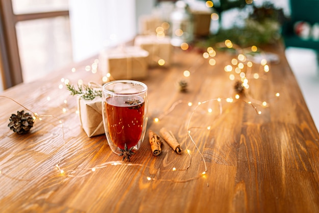 Glass mug of black tea with star anise on the wooden table with garland