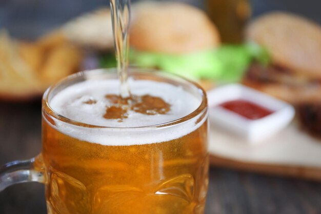 Photo glass mug of draft light beer with snacks on dark wooden table close up