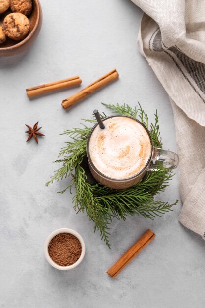 Foto coppa di cioccolato caldo con panna montata su un supporto con rami di pino su uno sfondo chiaro con biscotti a bastone di cannella, cucchiaio di anice e polvere di cacao