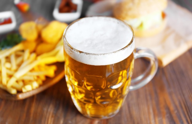 Glass mug of light beer with French fries on dark wooden table close up