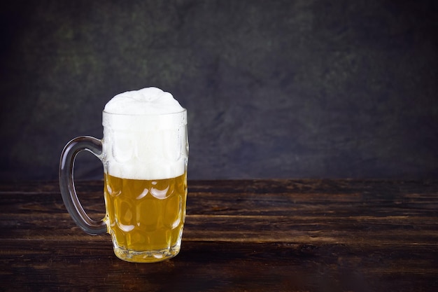 Glass mug with beer and white foam on brown wooden table