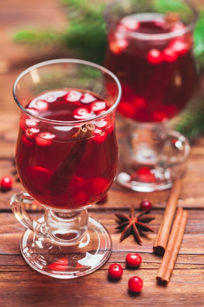 Glass of mulled wine with cranberry and scented cinnamon sticks on a wooden table