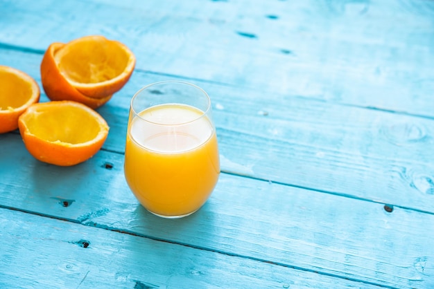 파란색 나무 테이블에 다이어트를 위해 일부는 통째로, 일부는 짜낸 여러 유기농 오렌지의 천연 주스 한 잔. 건강한 아침 식사
