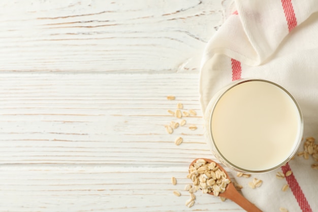 Glass of oat milk, spoon with oatmeal seeds and napkin on white