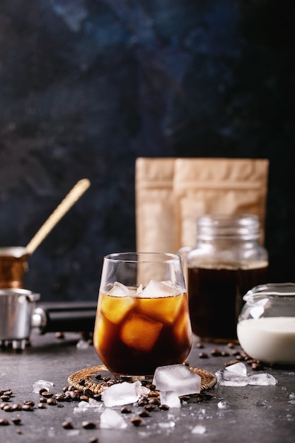 사진 어두운 벽 위에 크림, 구리 cezve 및 커피 원두와 함께 제공되는 얼음 조각이있는 아이스 커피 한잔