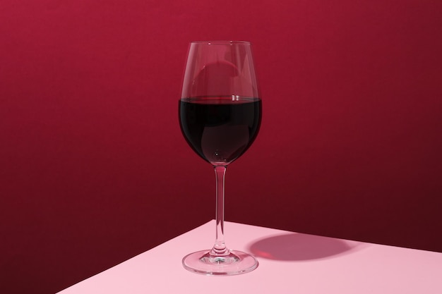 Бокал вина на розовом столе на малиновом фоне