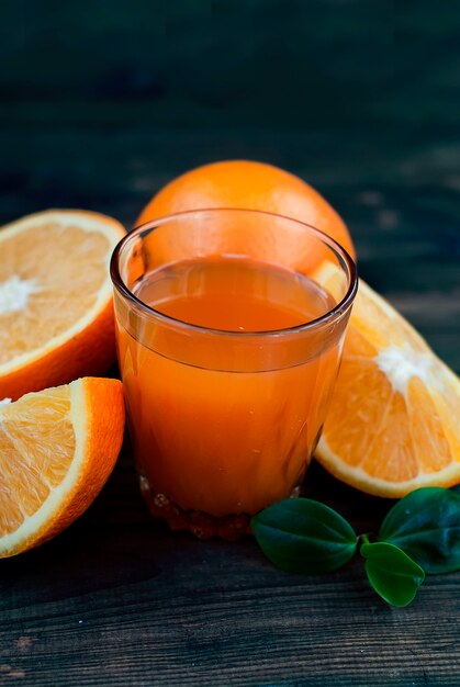 Glass of orange juice and a group of oranges on dark board