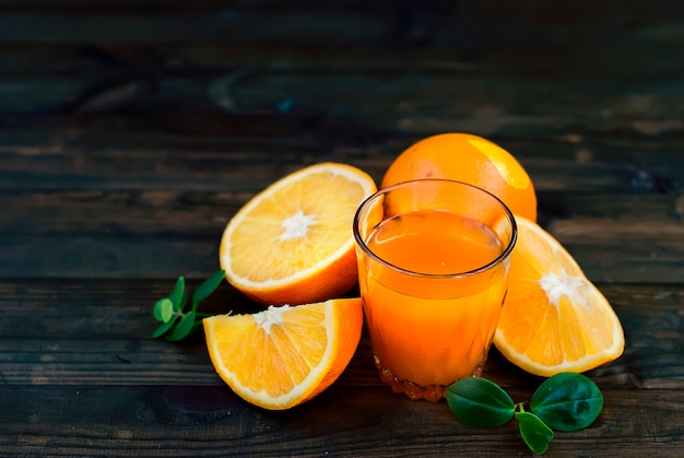 Стакан апельсинового сока и группа апельсинов на темной доске