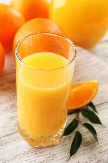 Glass of orange juice and oranges on color wooden table background