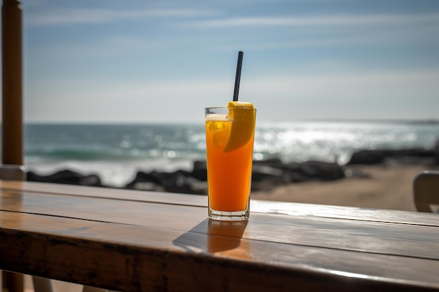 A glass of orange juice sits on a table overlooking the ocean.