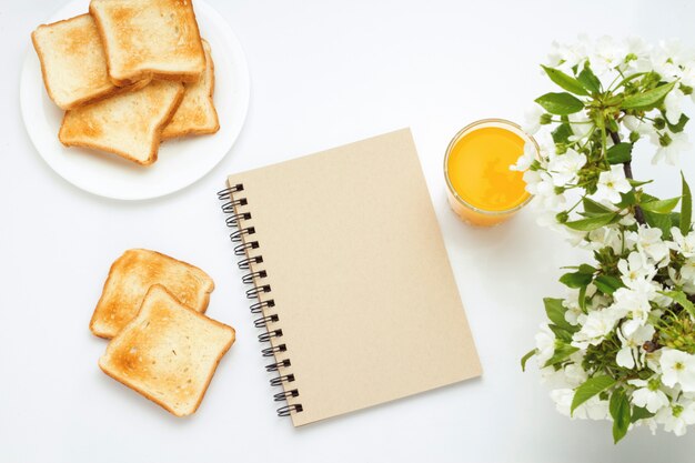 Glass of orange juice, Toasts on a white plate, Notepad and a Branch with Flowers on a white background. Concept of a healthy spring breakfast