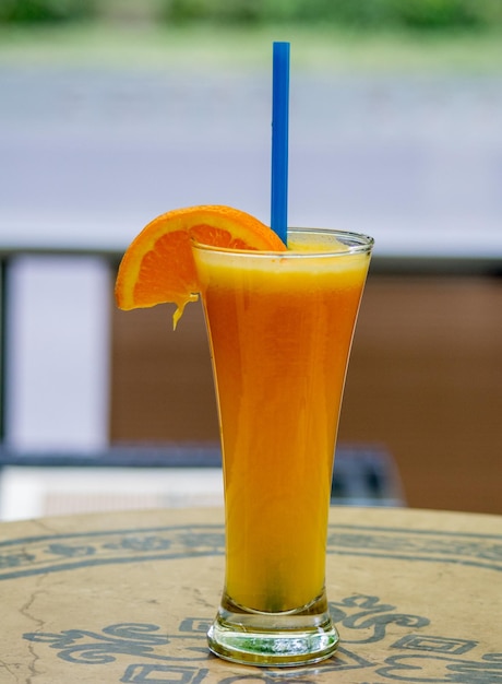 A glass of orange juice with a blue straw on top of it.