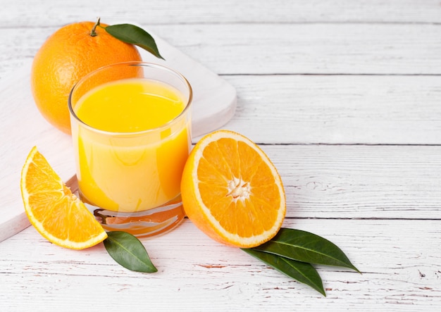 Foto vetro del succo di frullato arancio fresco organico con le arance crude su fondo di legno bianco