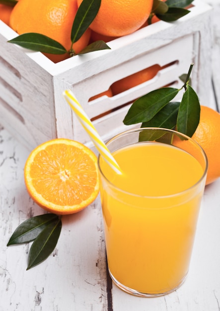 Foto bicchiere di succo d'arancia fresco organico con arance crude in scatola di legno bianca