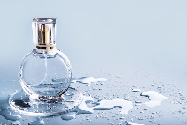 Bottiglia di profumo in vetro e gocce d'acqua su sfondo blu fragranza invernale o primaverile