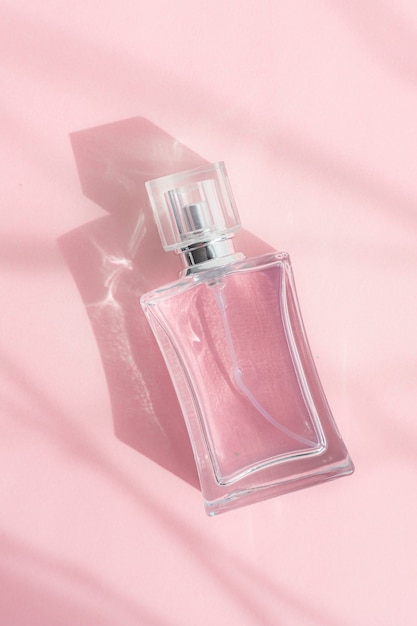 A glass perfume bottle on a pink background with sunlight and shadows