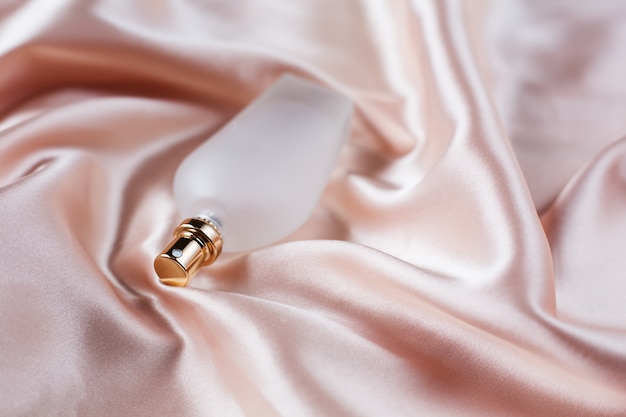 Glass of perfume over pink background