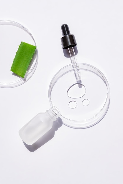 Piatto di petri in vetro con gocce di gel di aloe per il viso e flacone contagocce di retinolo o siero idratante olio essenziale con estratti di erbe prodotti cosmetici dermatologia scienza laboratorio cosmetico