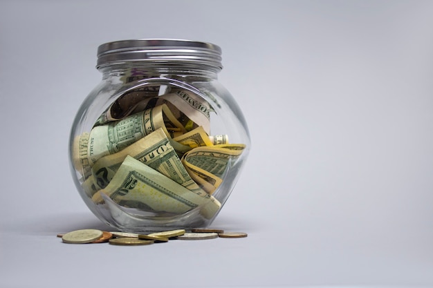 Glass piggy bank with dollars and euro on a gray background.