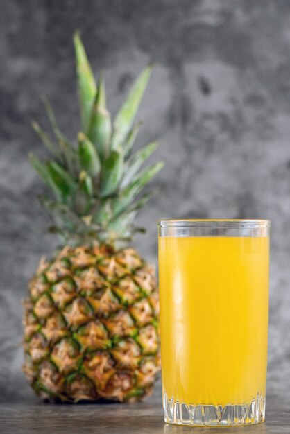 Photo glass of pineapple juice with fresh fruits on grey bacground