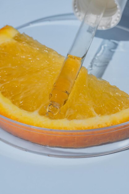 Стеклянная пипетка кислоты AHA на апельсине в стеклянном круге чашка Петри синий фон Концепция косметики