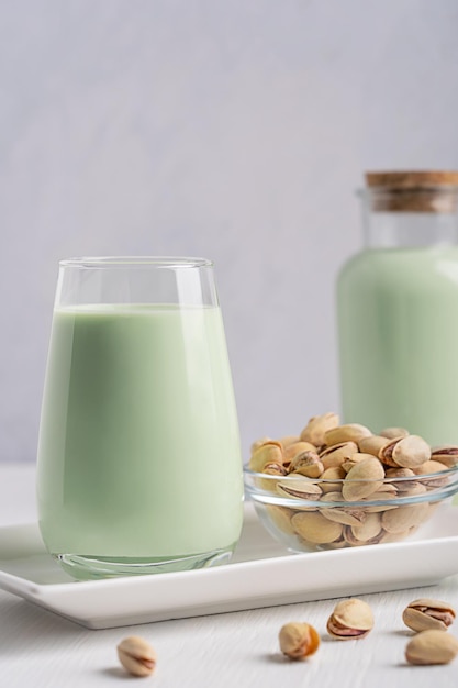 Glass of pistachio plant based vegan milk served with seeds on plate on white wooden table