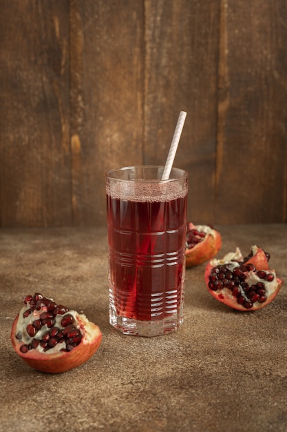 A glass of pomegranate juice and red pieces of pomegranate fruit on brown wooden background, vertical