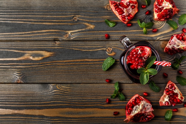 Glass of pomegranate juice with fresh pomegranate fruits and mint on wooden table.