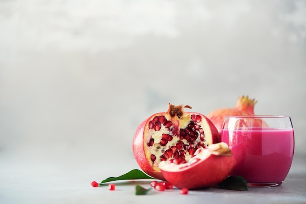 Glass of pomegranate juice with ripe pomegranate fruit on grey concrete background Banner with copy space Vegan healthy diet concept