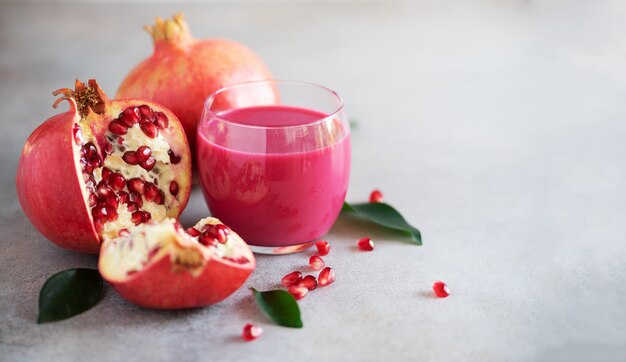 Glass of pomegranate juice with ripe pomegranate fruit on grey concrete background. 