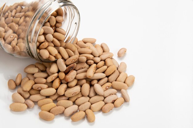 Glass pot with beans pouring out in a white background