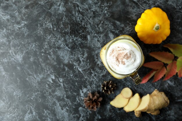 Glass of pumpkin latte and ingredients on black smokey table