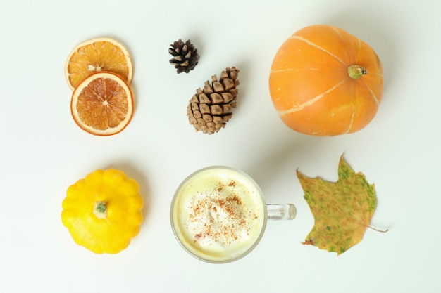 Glass of pumpkin latte and ingredients on white background