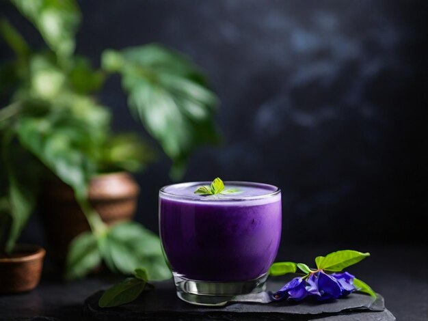 a glass of purple liquid sits on a table with a plant in the background