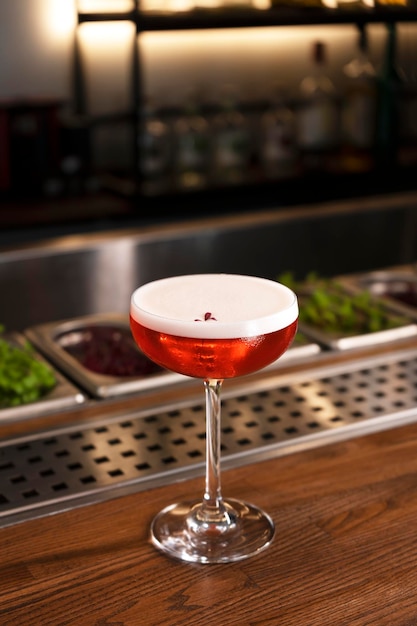 A glass of red alcohol drink with foam and flower petal cocktail garnish vertical orientation